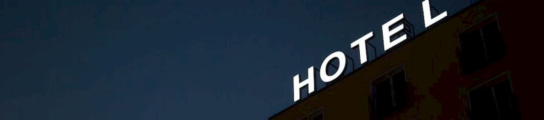 A building facade with a glowing sign reading &ldquo;HOTEL&rdquo; against a dark evening sky.