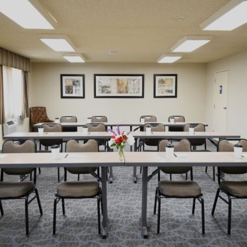 A bright conference room with rows of chairs around a long table, framed pictures on the walls, and a flower centerpiece in the center.