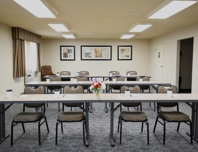 A bright conference room with rows of chairs around a long table, framed pictures on the walls, and a flower centerpiece in the center.
