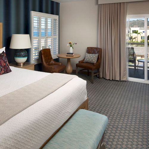 A hotel room with a large bed, seating area by a window, and a balcony view, neutral tones, and soft lighting.