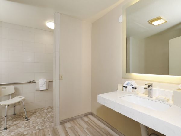 Modern hotel bathroom with a walk-in shower, tiled walls, vanity sink, and backlit mirror.