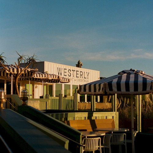 A sunny patio view of the Westerly Inn sign, cabanas and striped umbrellas against a cloudy blue sky.